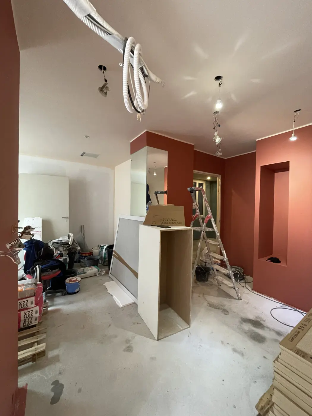 Pièce en travaux : murs peints, gaines apparentes au plafond et matériaux de chantier au sol